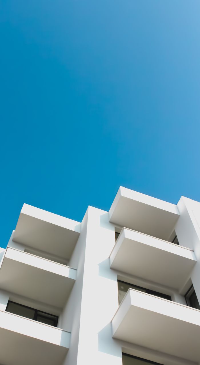 gallery-02 Low angle shot of a modern white building with balconies against a clear blue sky, showcasing architectural design.
